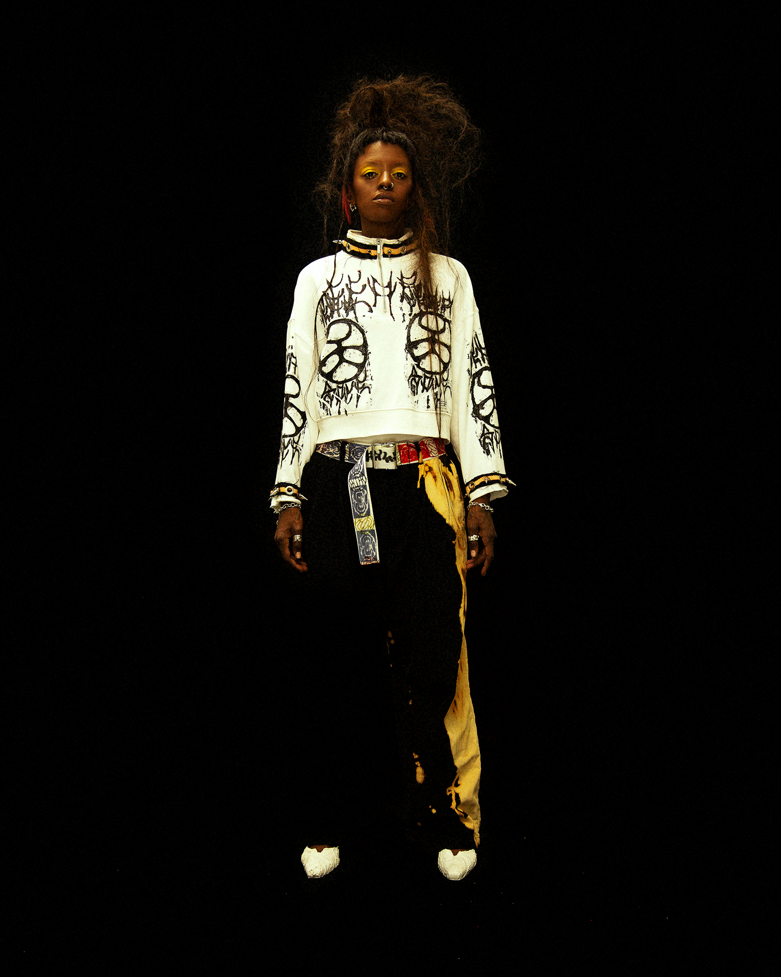 Full body shot of a model on black background wearing a white sweater, black pants and white heels